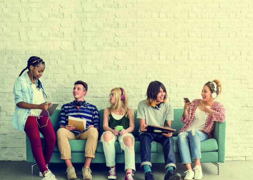 The picture shows 5 adults sitting on a sofa and talking with eachother.