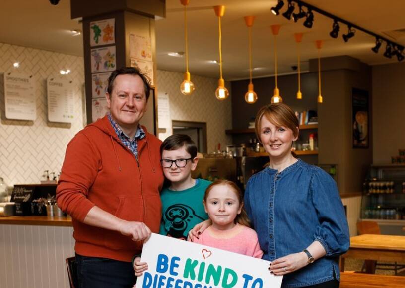 A family pose together while holding a 'Be kind to different minds' poster