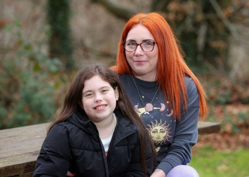 A mother and daughter smiling together while sitting at a park bench