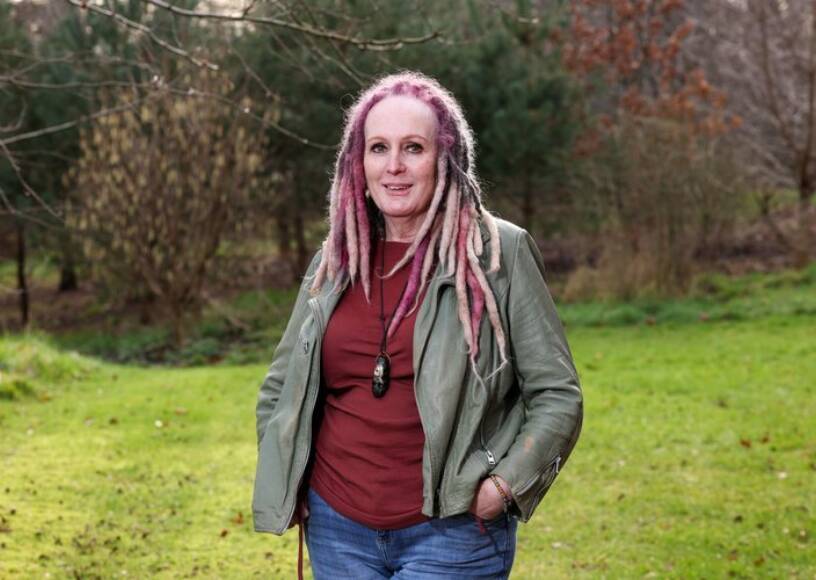 A woman smiles while standing in a grassy field