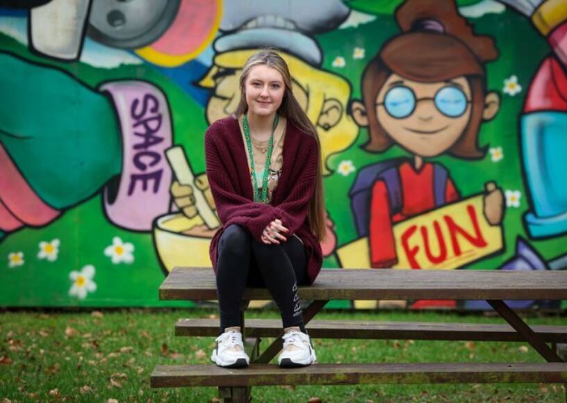 A young girl smiling and sitting on top of a picnic bench