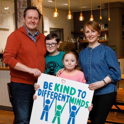 Family photographed together holding a 'be kind to different minds' poster