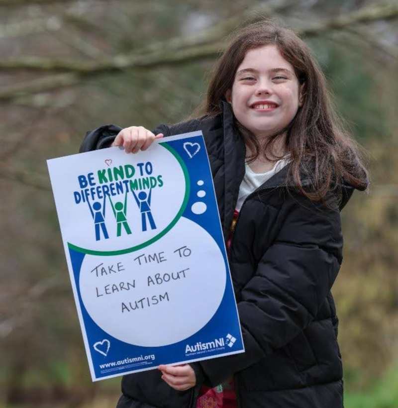 Autism NI member holding a 'Be kind to different minds' poster