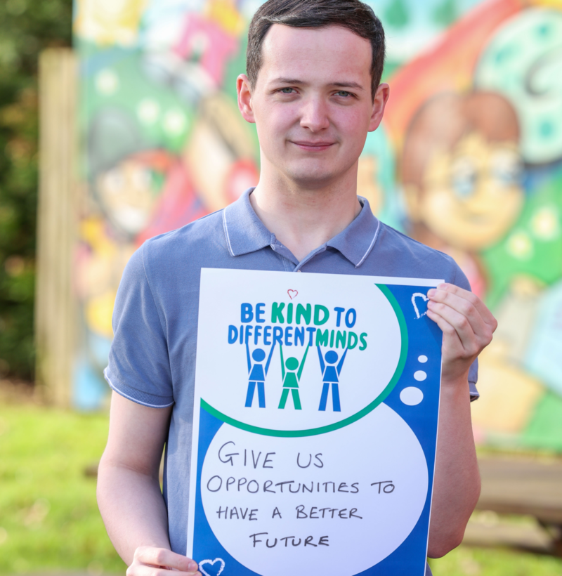 Autism NI member holding a 'Be kind to different minds' poster