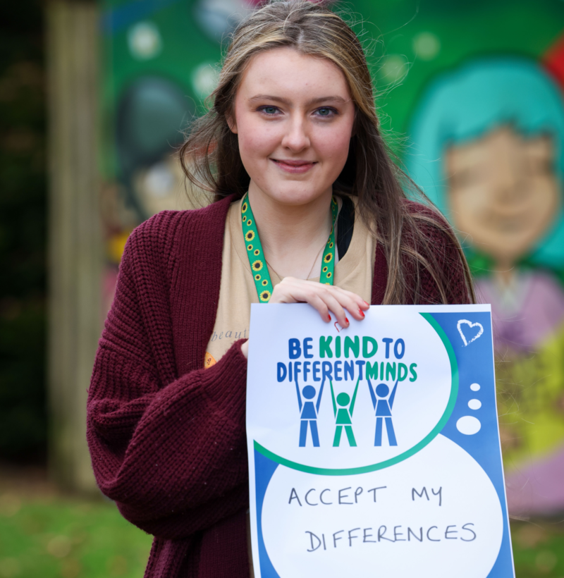 Autism NI member holding a 'Be kind to different minds' poster