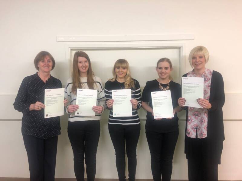 Several women smiling and holding AQA accreditation documents