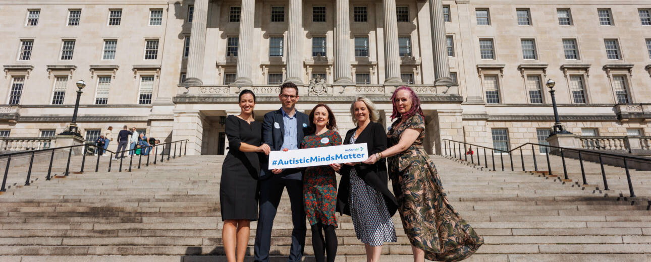 A group of people stand outside Stormont building holding a sign that reads '#AutisticMindsMatter'