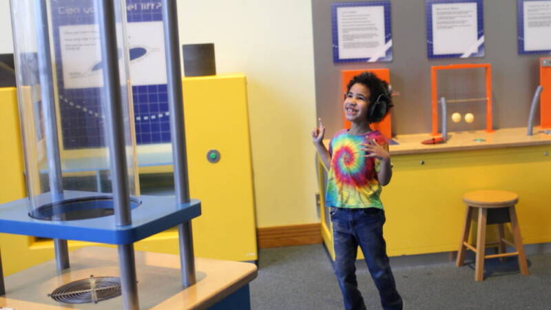 A young boy in a bright t-shirt, excitedly jumping while watching an air tunnel.
