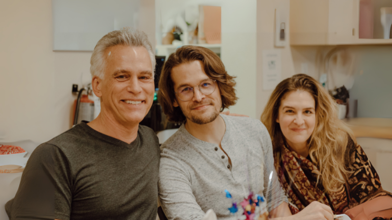 3 adults sitting beside each other smiling in a kitchen area