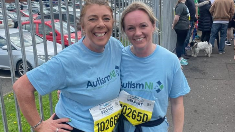 Two members of Autism NI smile together wearing marathon stickers