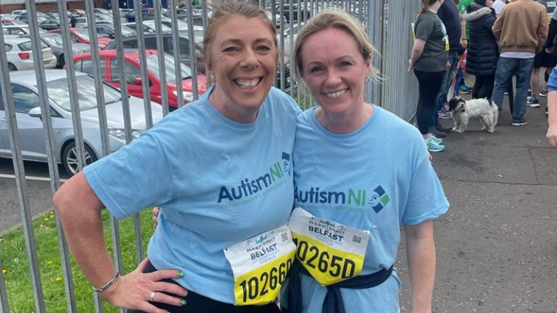 Two members of Autism NI smile together wearing marathon stickers