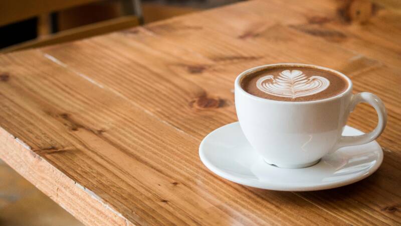 A coffee cup with a foam pattern on a wooden table