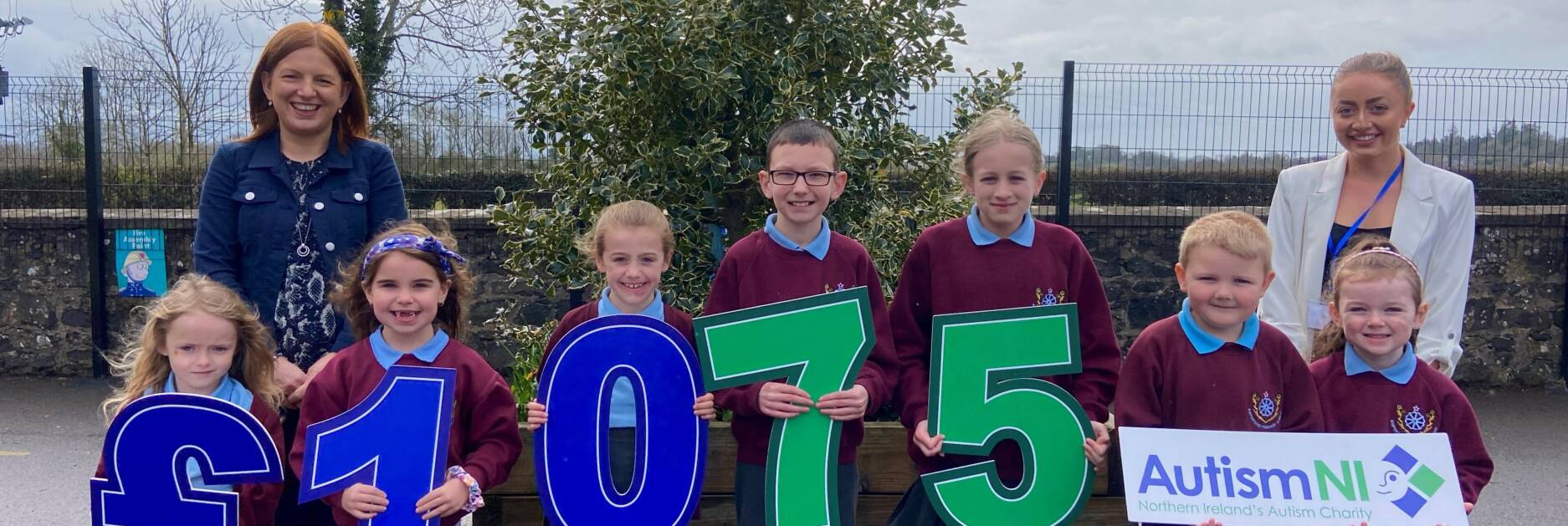 Staff and students of Ampertaine primary school smile and hold up signs that spell '£1075'