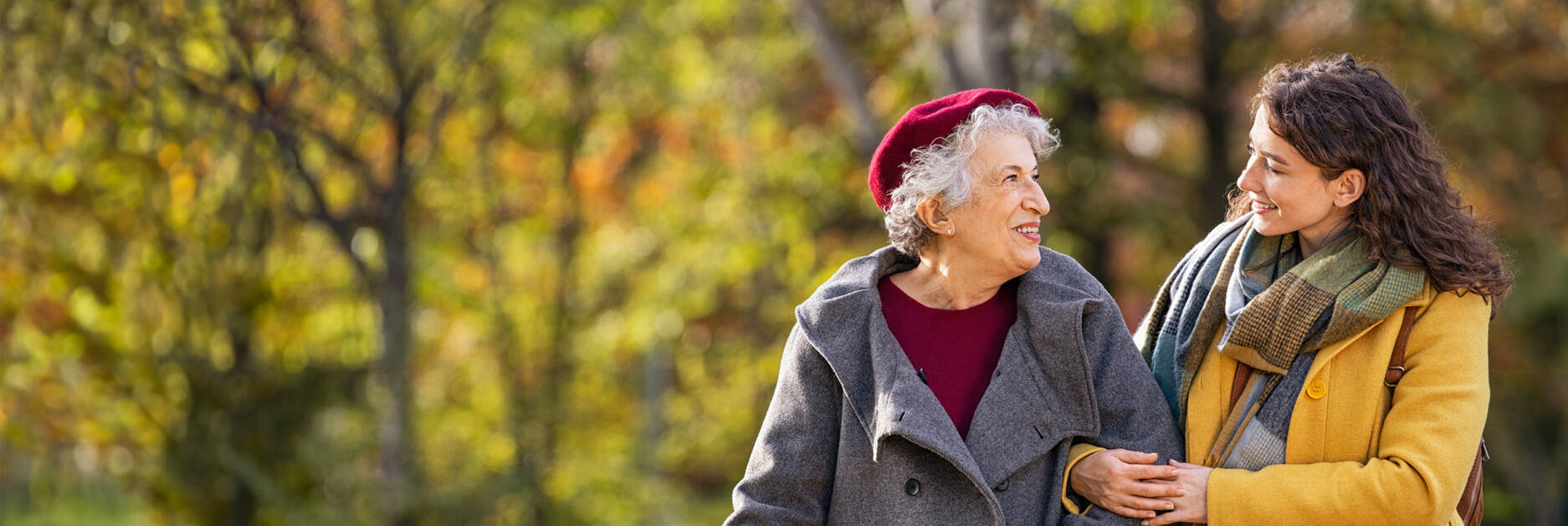 A young woman and an elderly woman walking with arms linked in a park