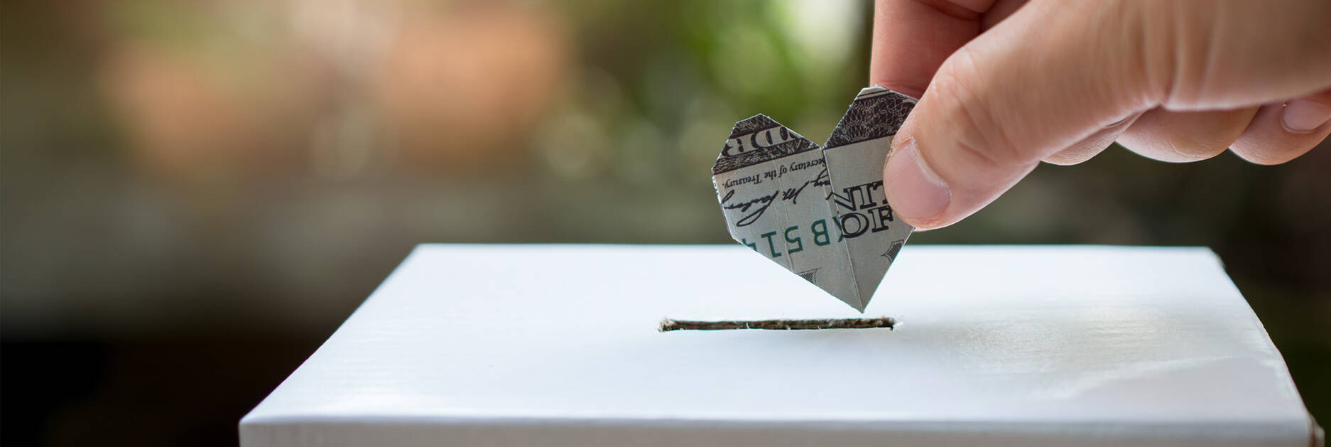 A person's hand dropping a note shaped into a heart into a paper box