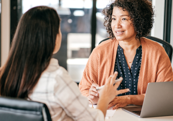 Two employees talking to each other across a table, with a laptop on the table.