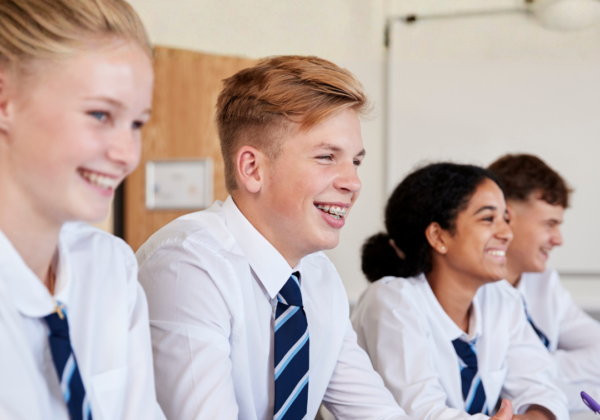 A row of four students in uniform sitting smiling while listening in class.