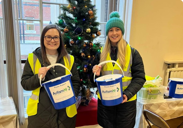 Autism NI volunteers wearing high-vis jackets and holding collection buckets in front of a Christmas tree
