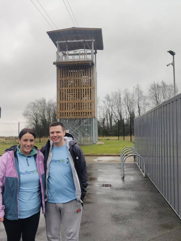 Two Autism NI members smile in front of a zipline tower