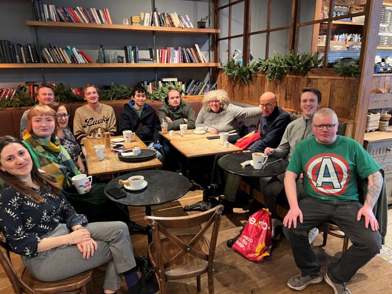 A group of people smile and pose sitting together in a café. These groups of people are part of Autism NI's Autistic Adult Support Network.