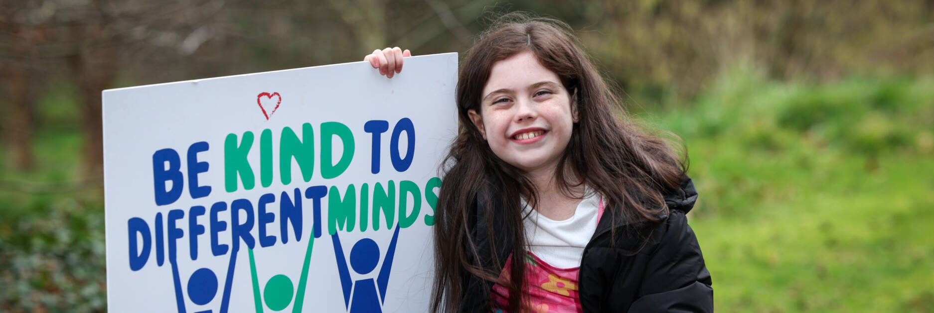 Autism NI member posing with a 'Be kind to different minds' poster