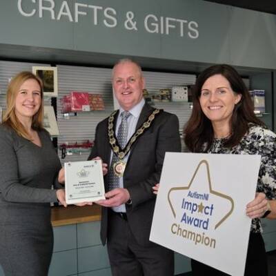 Several people smile and pose together with an Autism NI impact award and impact award champion poster