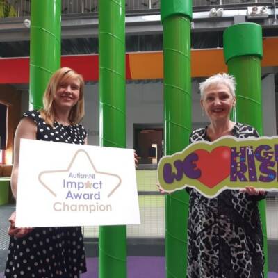 Two members of High Rise smile and pose with an Autism NI Impact Award Champion poster