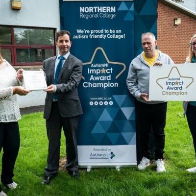 Members of Northern Regional College stand in front of an impact award champion poster and pose with their award