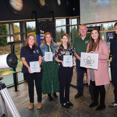 A group of people standing next to a telescope smiling and posing with a impact awards