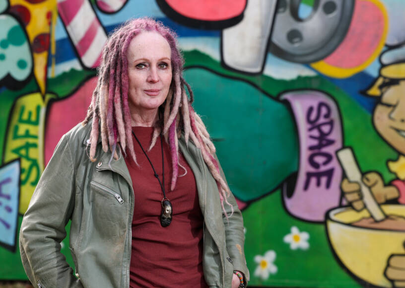 An autistic adult standing in front of a colourful wall.