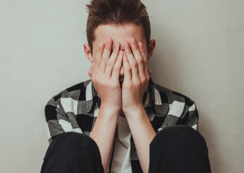 A teenage boy sitting on floor with his head in his hands, looking stressed.