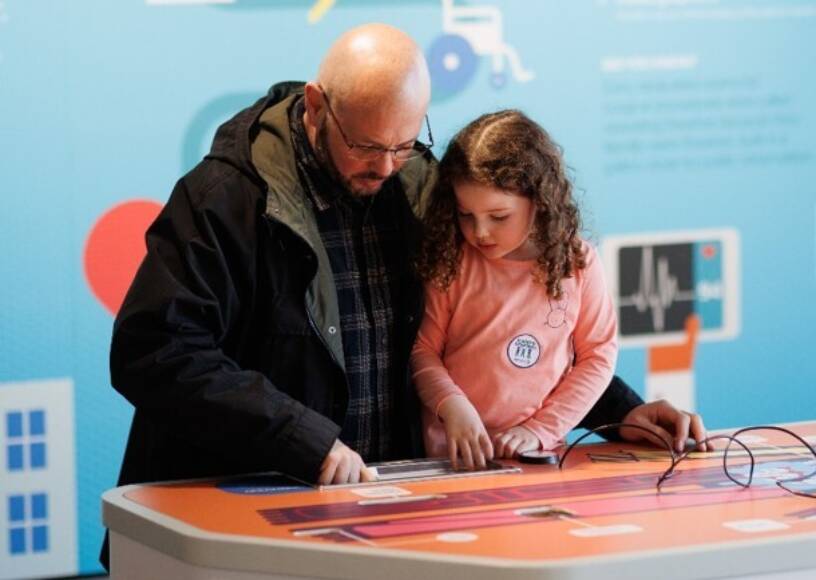 An adult and child stand closely together, looking down and working together to complete an activity