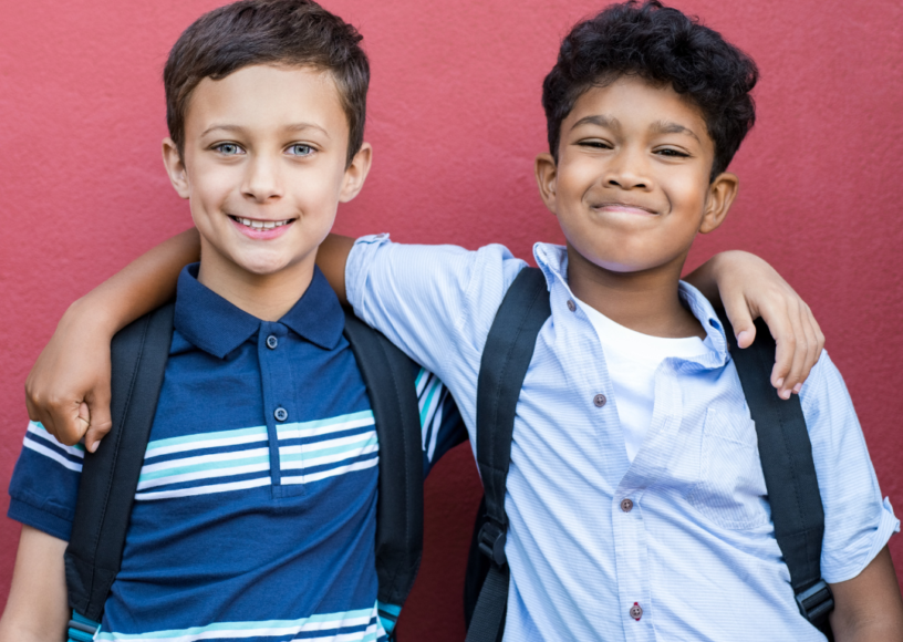 2 young boys with their arms around each other, looking happy and confident.