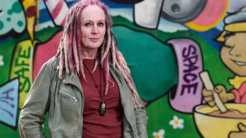 An autistic adult standing in front of a colourful wall.