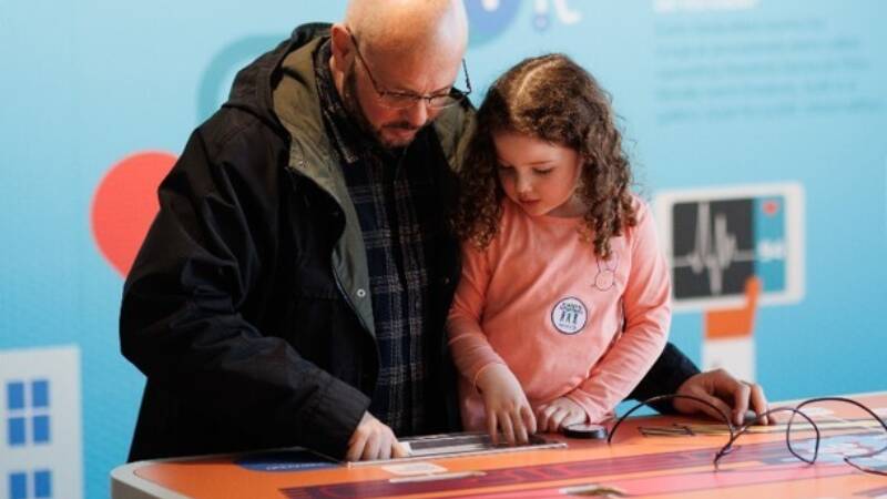 An adult and child stand closely together, looking down and working together to complete an activity