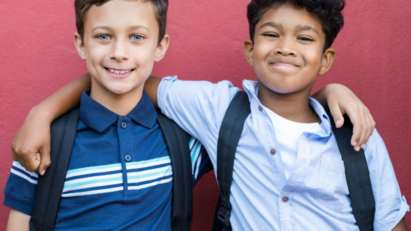 2 young boys with their arms around each other, looking happy and confident.
